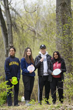 Four people stand in the woods at a disc golf course