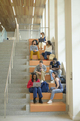 Eight students converse, in separate groups, on a brightly lit staircase 