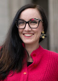 Marika Cifor, wearing a bright pink sweater, earrings, patterned glasses and smiling.