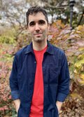 A photo of Ben Green standing outdoors in an autumn garden, wearing a navy jacket and red shirt.