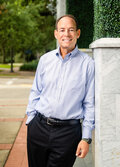 Photo of Dr. David J. Cooper, a man leaning against a stone fence, smiling. 