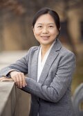 Sherry Li, wearing a grey suit jacket and white shirt, looking at the camera, smiling.