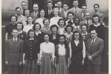 A black and white photo of the class of 1948, wearing skirts and crisp button-downs or suits, with more than 30 people