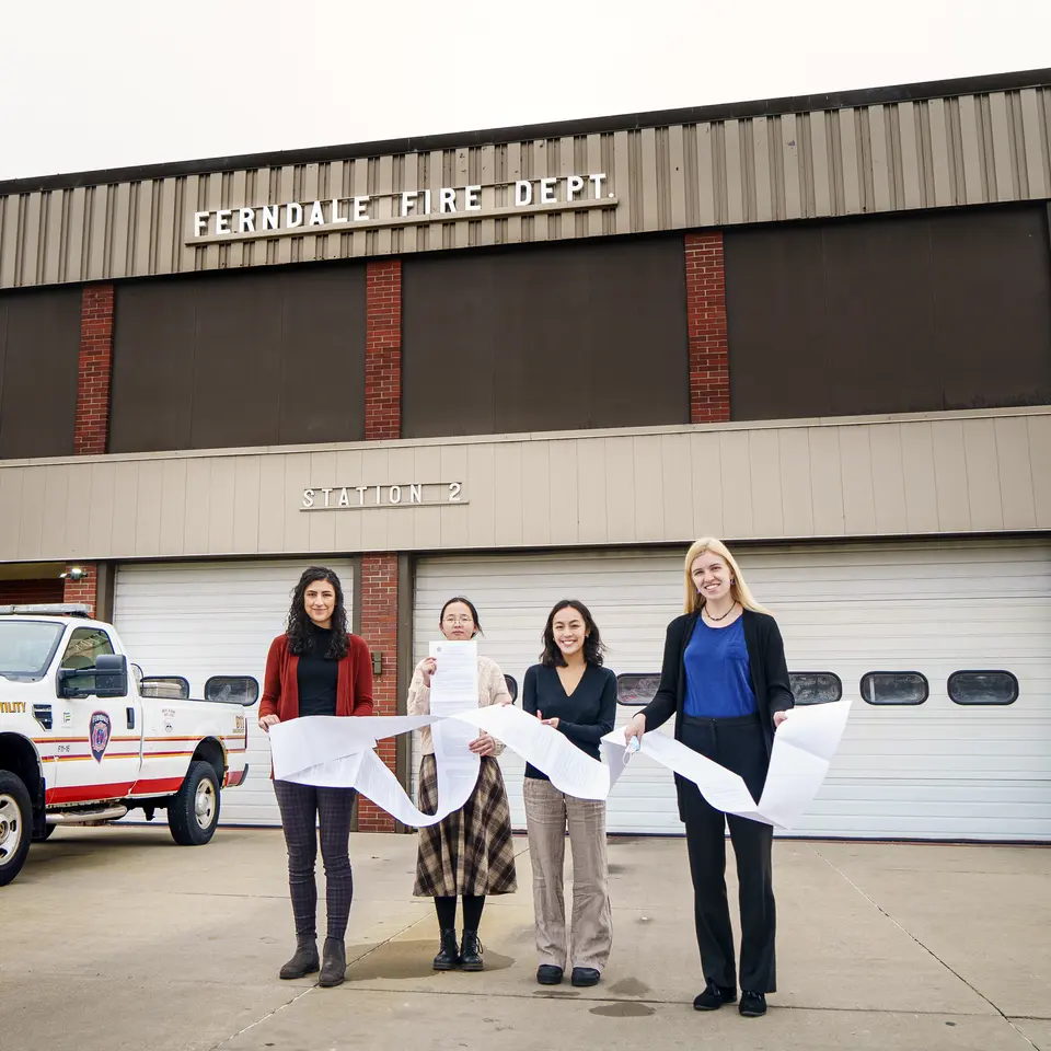 Four students hold a long document in front of a fire station in ferndale